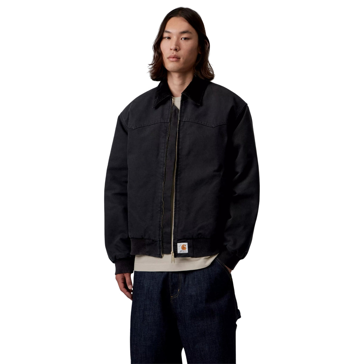 Casaco Carhartt WIP OG Santa Fe em Preto — modelo masculino de frente, meio corpo, lona Dearborn preta, gola em bombazine preta, fecho de correr dourado aberto, Square Label Carhartt WIP na bainha, corte Loose OG oversized, sweatshirt bege por baixo, calças cargo denim azul-escuro, fundo branco.