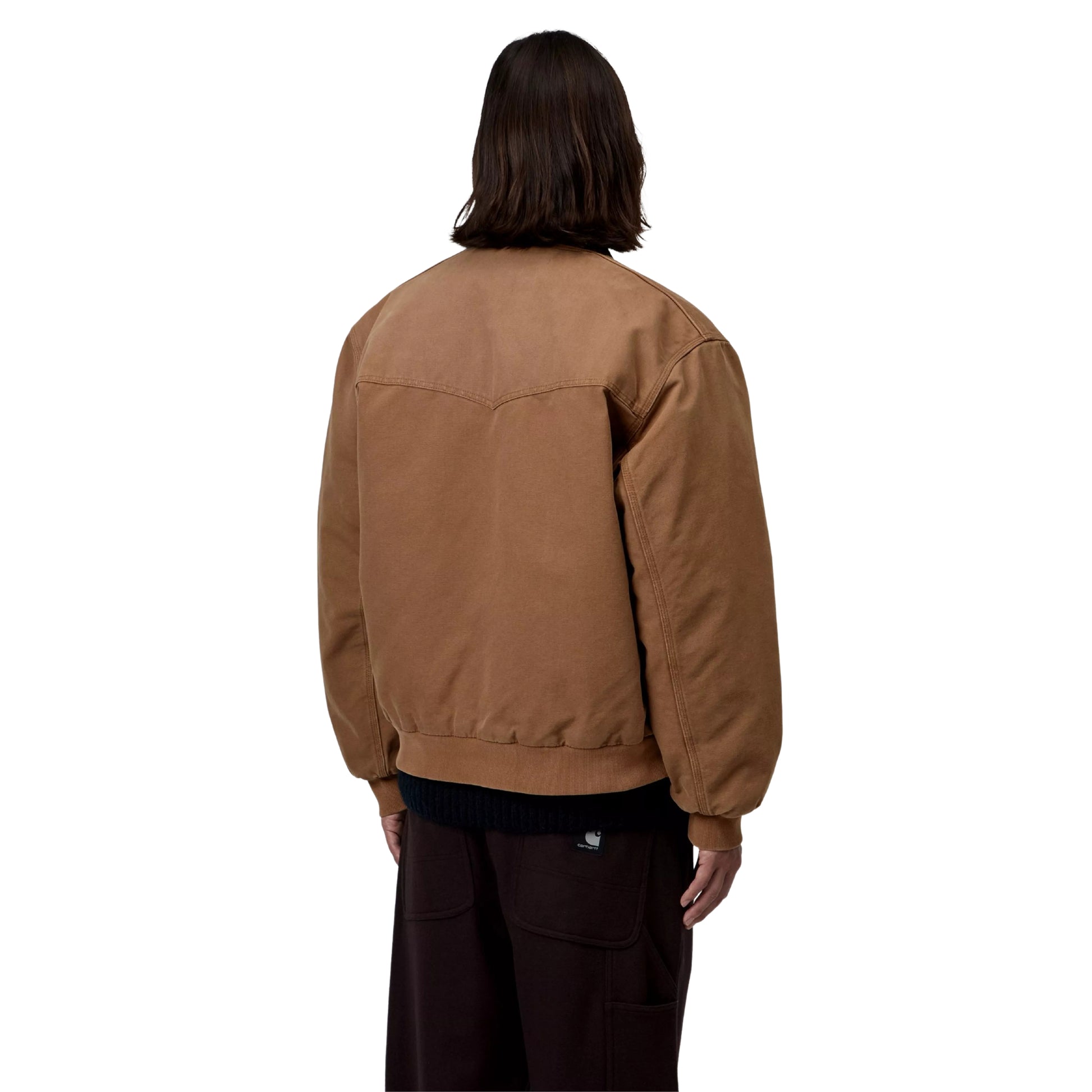 Casaco Carhartt WIP OG Santa Fe em WIP H Brown / Tobacco — modelo masculino de costas, meio corpo, lona Dearborn camel, costuras em arco no painel traseiro, faixa inferior em malha canelada camel, gola bombazine castanho-escuro, calças wide-leg bordeaux-escuro, fundo branco.