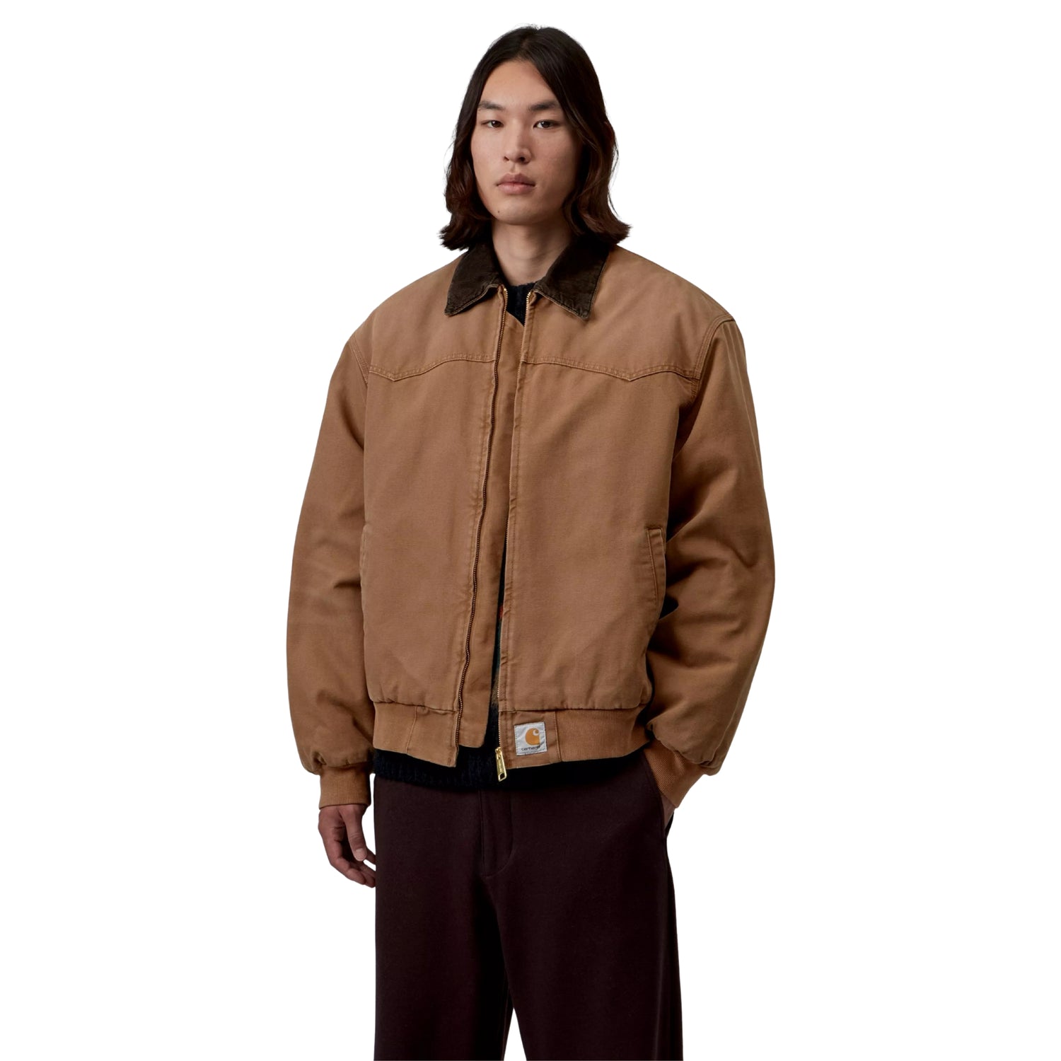 Casaco Carhartt WIP OG Santa Fe em WIP H Brown / Tobacco — modelo masculino de frente, meio corpo, lona Dearborn camel, gola bombazine castanho-escuro, fecho de correr dourado fechado, Square Label Carhartt WIP na bainha, corte Loose OG oversized, cabelo comprido escuro, calças wide-leg bordeaux-escuro, fundo branco.