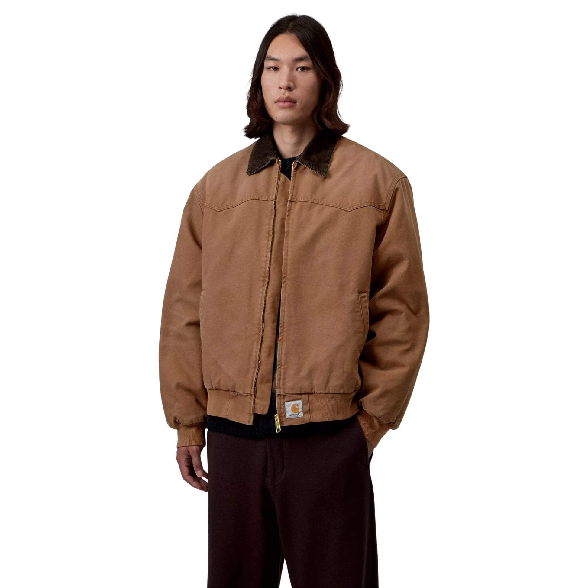 Casaco Carhartt WIP OG Santa Fe em WIP H Brown / Tobacco — modelo masculino de frente, meio corpo, lona Dearborn camel, gola bombazine castanho-escuro, fecho de correr dourado fechado, Square Label Carhartt WIP na bainha, corte Loose OG oversized, cabelo comprido escuro, calças wide-leg bordeaux-escuro, fundo branco.