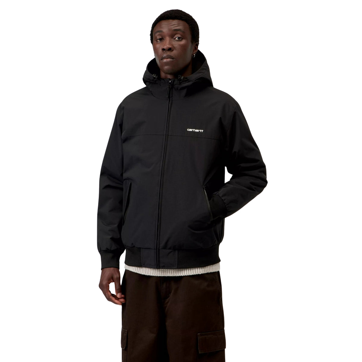 Casaco com carapuço Carhartt WIP Hooded Sail em Preto/Branco, vista frontal em plano médio no modelo, com fecho fechado até ao pescoço, logótipo branco no peito e uma mão no bolso lateral.