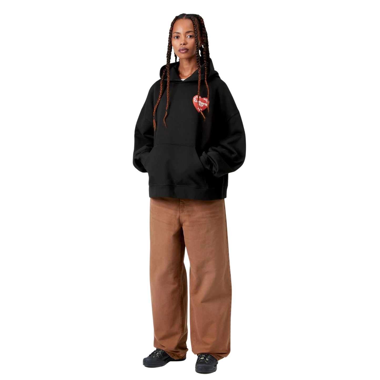 Camisola com capuz Carhartt WIP W' Hooded Hartt Case Sweat em Black — modelo feminino de frente, corpo inteiro, tranças longas, gráfico Hartt Case no peito esquerdo, bolso de canguru frontal, capuz volumoso, calças wide-leg cor de camel Carhartt WIP, sapatilhas pretas de sola grossa, malha de algodão escovada preta, fundo branco.