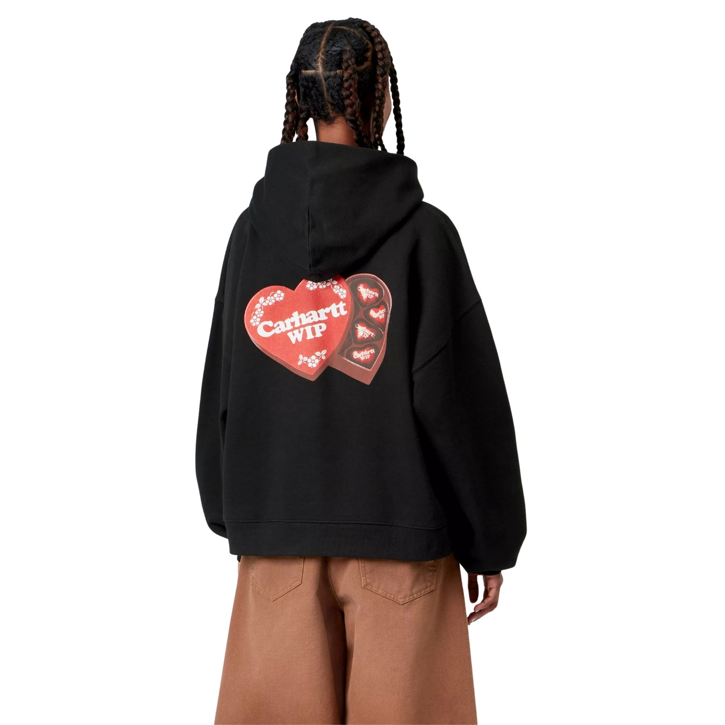 Camisola com capuz Carhartt WIP W' Hooded Hartt Case Sweat em Black — modelo feminino de costas, meio corpo, tranças longas, gráfico Hartt Case impresso nas costas: caixa de chocolates em formato de coração aberta a revelar bombons individuais com logótipo Carhartt WIP em creme, fundo vermelho e bordado floral bege, calças wide-leg cor de camel, malha de algodão escovada preta, fundo branco.