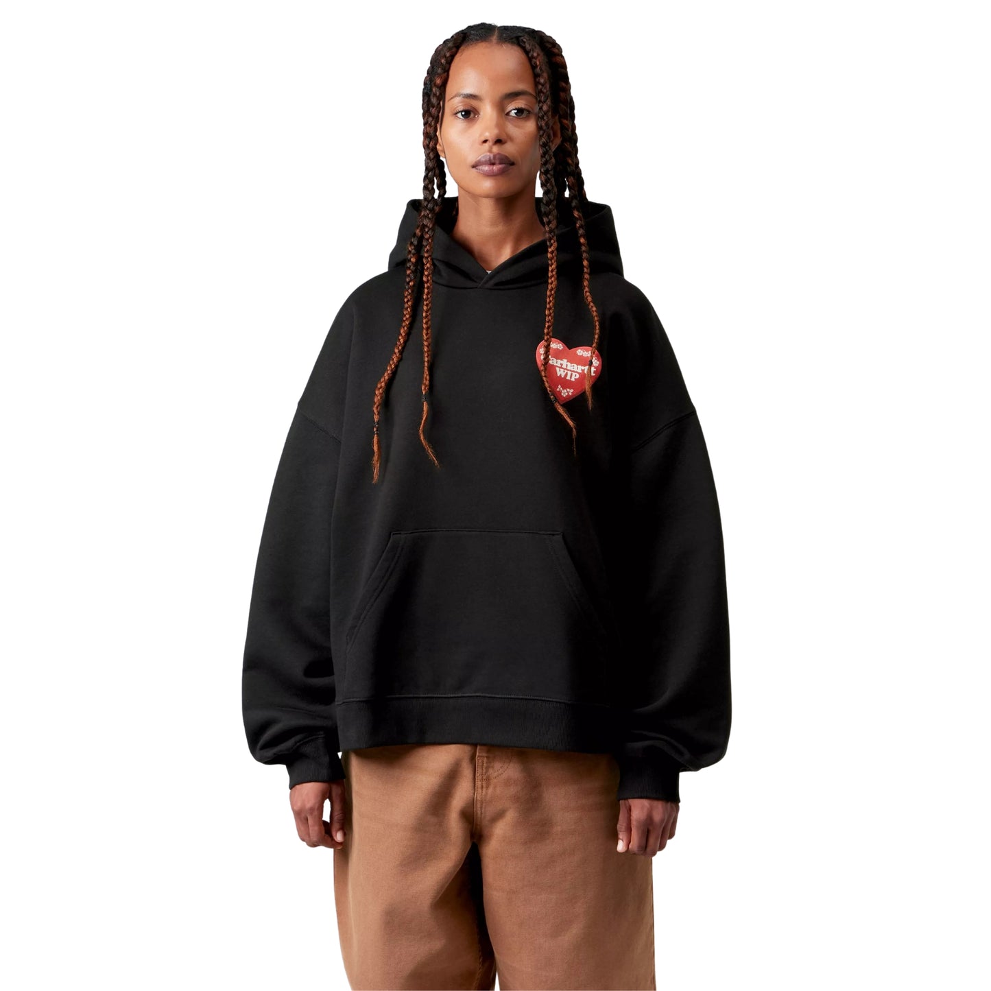 Camisola com capuz Carhartt WIP W' Hooded Hartt Case Sweat em Black — modelo feminino de frente, meio corpo, tranças longas, gráfico Hartt Case impresso no peito esquerdo: tampa de caixa de chocolates em formato de coração vermelho com texto "Carhartt WIP" em creme e motivos florais bege, bolso de canguru frontal, capuz volumoso, calças wide-leg cor de camel, malha de algodão escovada preta, fundo branco.