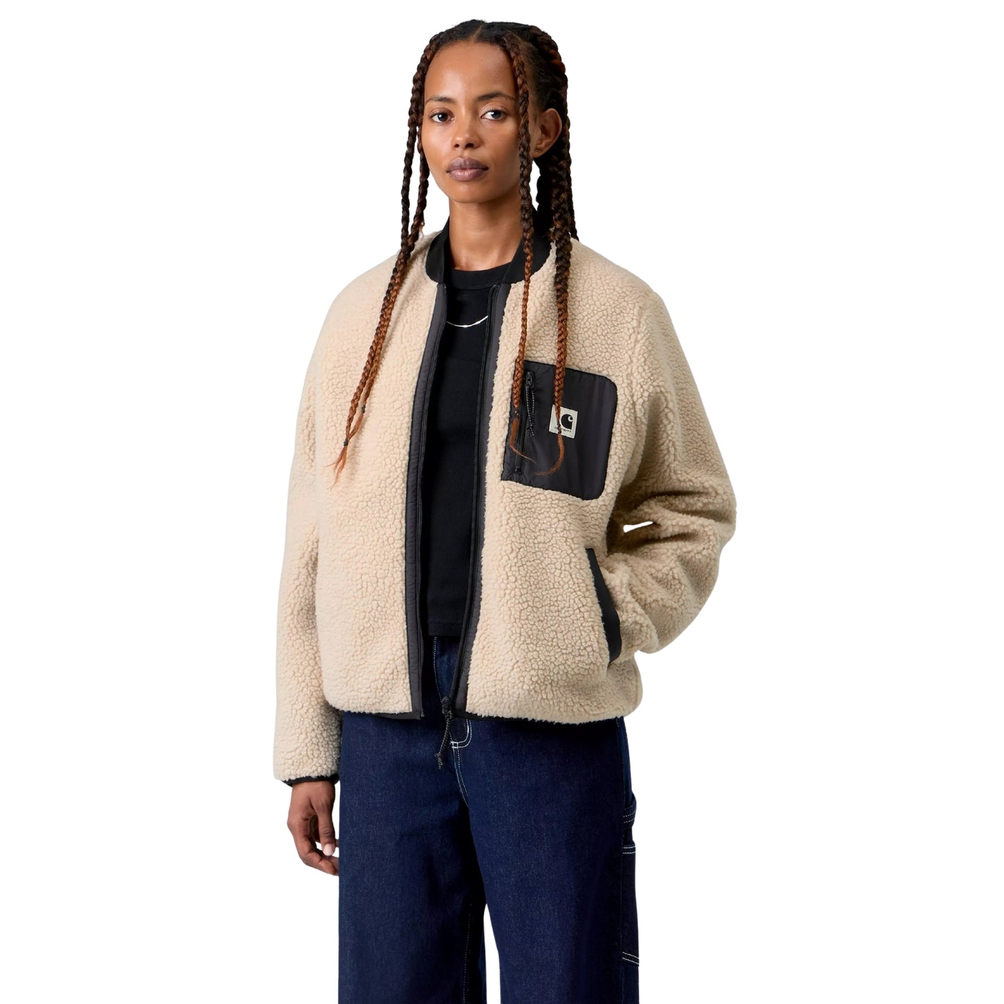 Casaco polar Carhartt WIP W' Janet Liner em Fleur De Sel / Black — modelo feminino de frente, meio corpo, tranças longas, casaco aberto sobre t-shirt preta, pile de poliéster texturado bege areia Fleur de Sel, gola canelada preta, bolso de peito esquerdo em tafetá de nylon preto com fecho de correr e etiqueta Square Label Carhartt, bolso lateral com debrum preto visível, calças wide-leg denim azul-escuro Carhartt WIP, fundo branco.