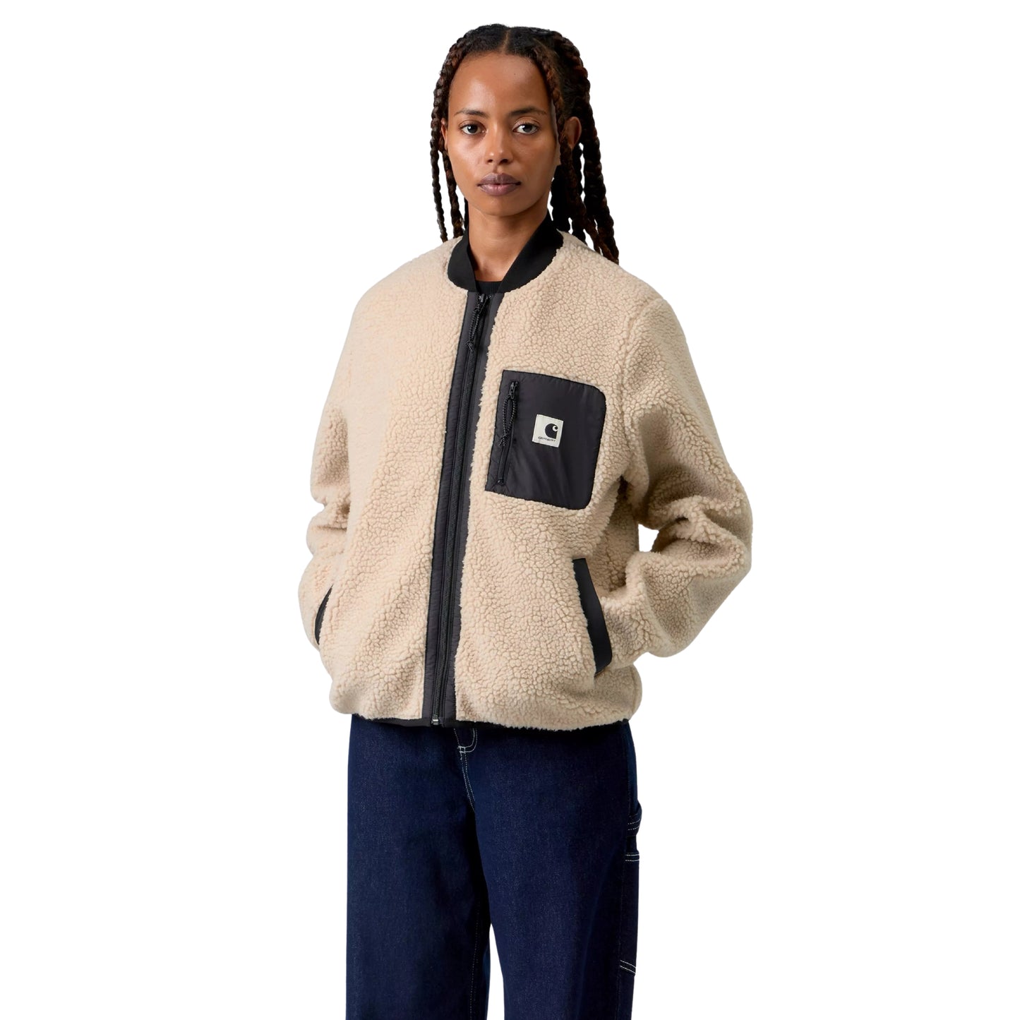 Casaco polar Carhartt WIP W' Janet Liner em Fleur De Sel / Black — modelo feminino de frente, meio corpo, tranças longas, casaco fechado, pile de poliéster texturado bege areia Fleur de Sel, gola canelada preta, fecho de correr frontal preto, bolso de peito esquerdo em tafetá de nylon preto com etiqueta Square Label Carhartt e puxador de fecho preto, bolsos laterais com debrum preto e mãos nos bolsos, calças wide-leg denim azul-escuro, fundo branco.