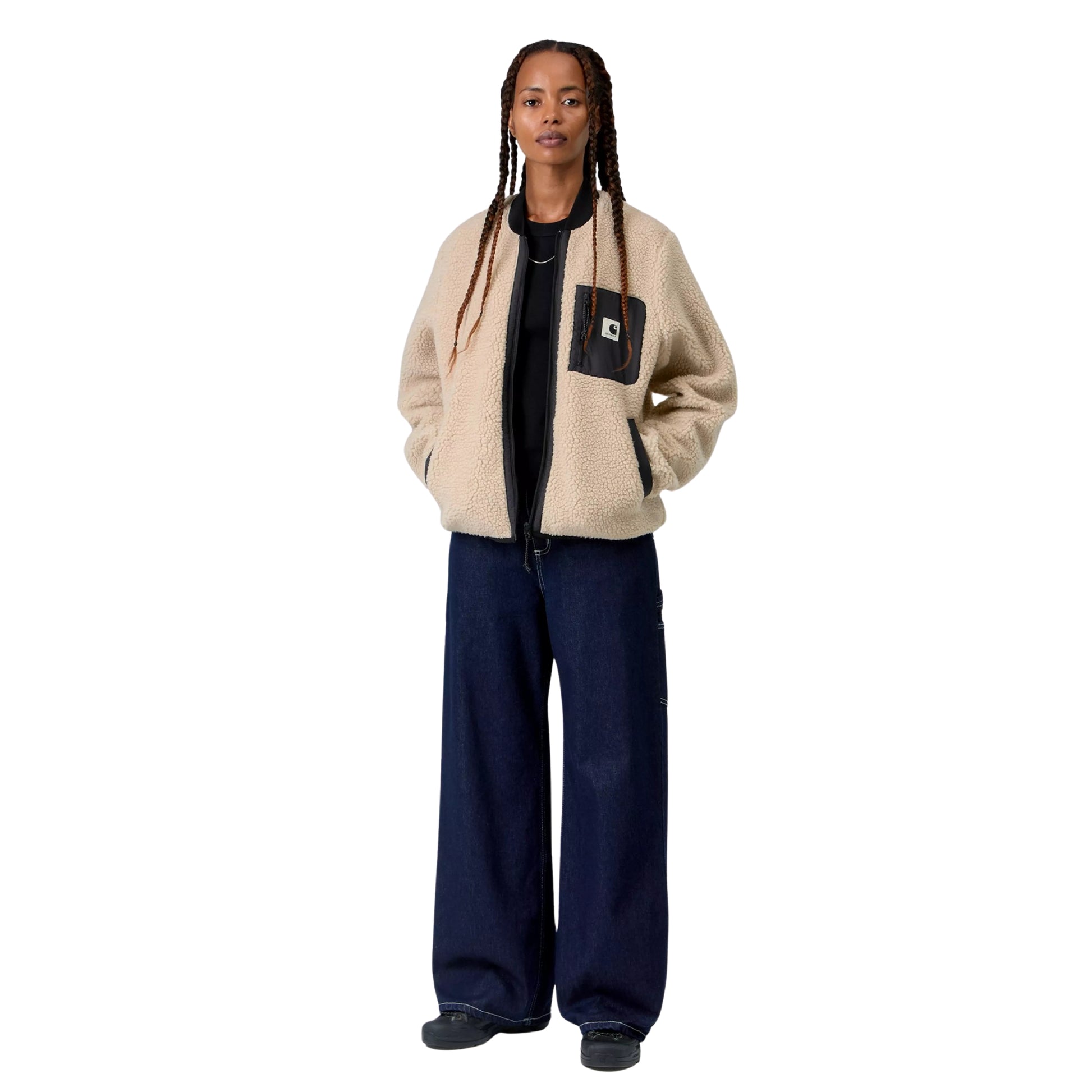 Casaco polar Carhartt WIP W' Janet Liner em Fleur De Sel / Black — modelo feminino de corpo inteiro, tranças longas, casaco aberto sobre t-shirt preta, pile de poliéster texturado bege areia Fleur de Sel, bolso de peito em tafetá de nylon preto com puxador de fecho e etiqueta Square Label Carhartt, bolsos laterais com debrum preto, calças wide-leg denim azul-escuro Carhartt WIP com costuras brancas, sapatilhas pretas, fundo branco.
