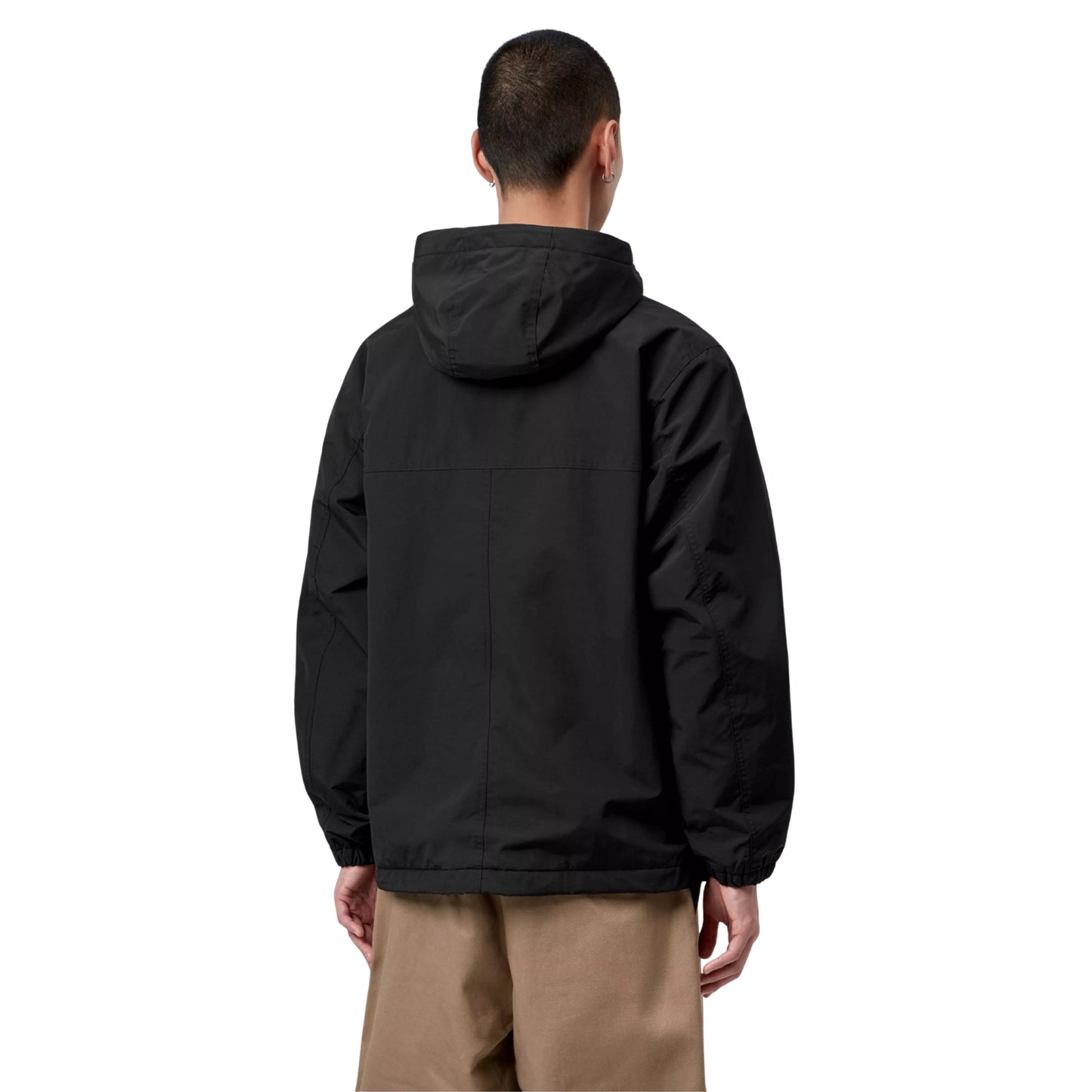 Anorak Carhartt WIP Windbreaker Pullover em Black / White — modelo masculino de costas, cabelo curto escuro, brinco pequeno visível, capuz volumoso preto, costas lisas sem gráfico com costuras estruturais, punhos elásticos, bainha com cordão de ajuste e puxador preto, calças wide-leg bege Carhartt WIP, nylon Supplex® preto Black, fundo branco.