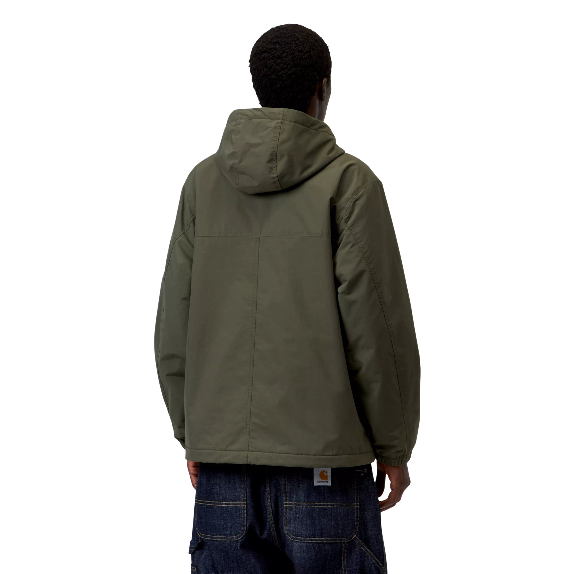 Anorak Carhartt WIP Windbreaker Pullover em Cypress / Black — modelo masculino de costas, gorro preto, capuz volumoso em Cypress, costas lisas sem gráfico com costuras estruturais visíveis, punhos elásticos, bainha com cordão de ajuste preto, etiqueta Carhartt WIP laranja na cintura das calças cargo denim azul-escuro largas, nylon Supplex® verde militar Cypress, fundo branco.