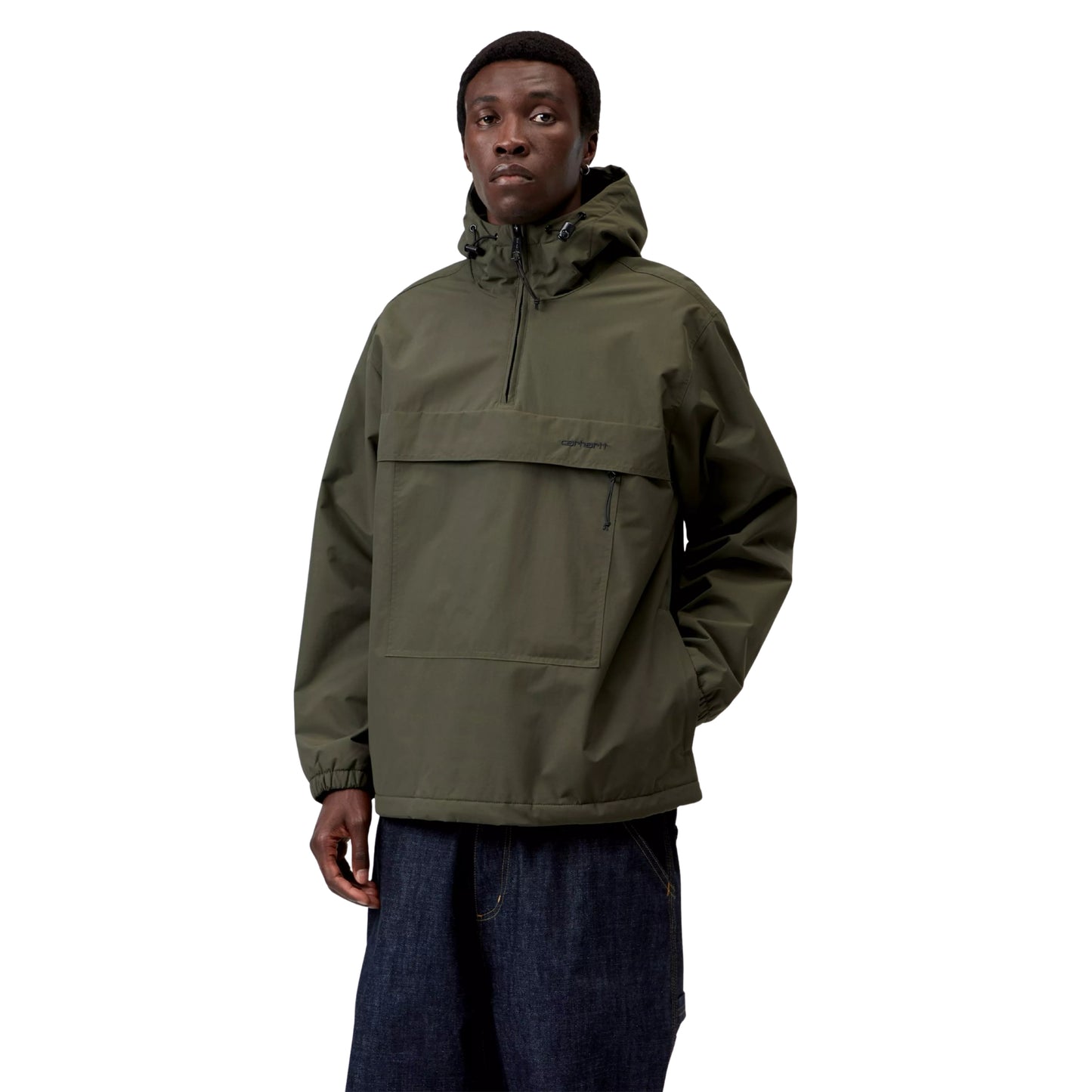 Anorak Carhartt WIP Windbreaker Pullover em Cypress / Black — modelo masculino de frente, meio corpo, gorro preto, capuz levantado com cordão e ajustador plástico preto, fecho de correr a meio do peito em Black, logótipo "carhartt." impresso no bolso frontal, bolso lateral com puxador de fecho preto visível, punhos elásticos, nylon Supplex® verde militar Cypress, fundo branco.