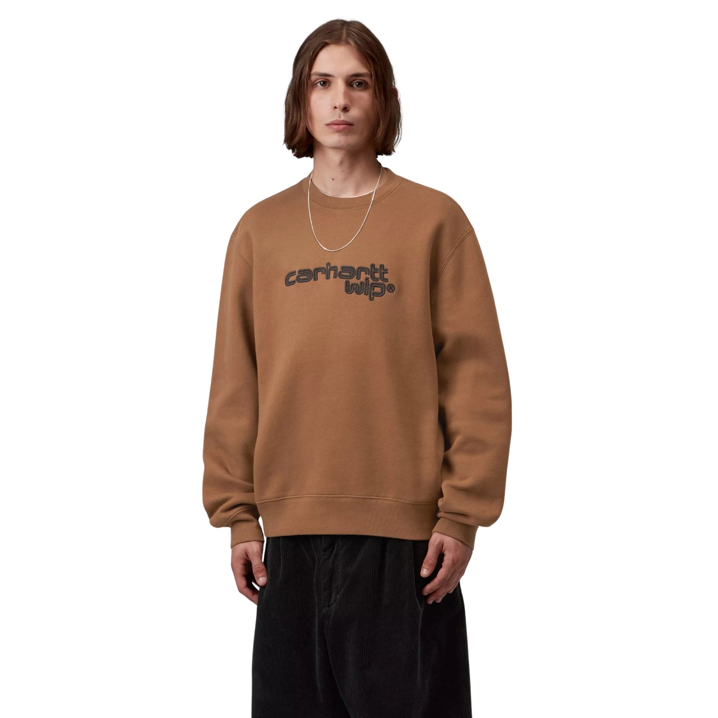 Camisola Carhartt WIP Wireless Sweat em Hamilton Brown / Black — modelo masculino de frente, meio corpo, cabelo comprido castanho, fio de ouro fino ao pescoço, detalhe do bordado "carhartt wip®" ao peito em tipografia arredondada com duplo contorno preto, malha de algodão escovada castanha Hamilton Brown, calças wide-leg bombazine preto, fundo branco.