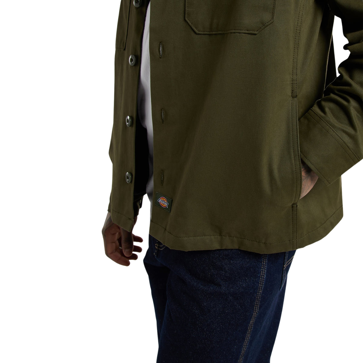 Casaco Dickies 247 em Deep Depths, close-up da parte inferior no modelo, mostrando o bolso lateral com a mão no interior, os botões e a etiqueta Dickies acima da bainha.