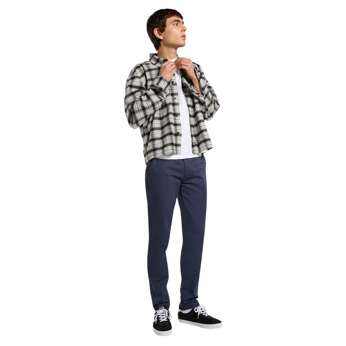 Calças Dickies 247 Slim Work Pant em Dark Navy — modelo de corpo inteiro, look completo com camisa de flanela xadrez branca e cinzenta, t-shirt branca por baixo, calças azul-marinho escuro de corte slim e sapatilhas skate pretas, fundo branco.