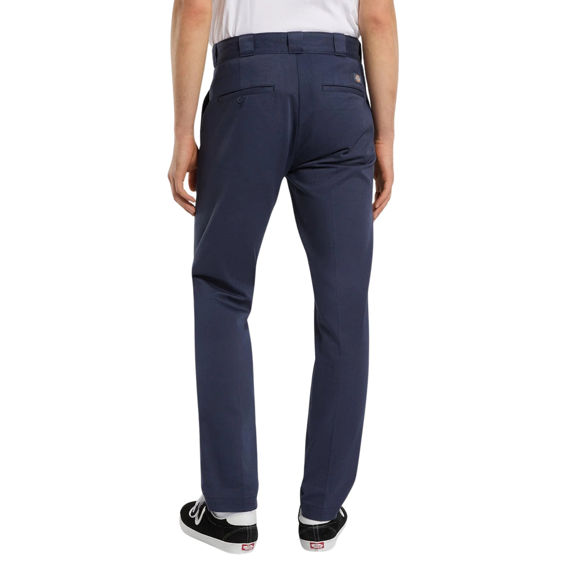Calças Dickies 247 Slim Work Pant em Dark Navy — modelo de costas, cintura aos pés, calças azul-marinho escuro de corte slim, passadores para cinto, bolsos traseiros ribeteados, sapatilhas skate pretas com atacadores brancos, fundo branco.