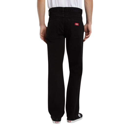 Calças de ganga Dickies 983 Regular Straight em Black Wash — modelo de costas, enquadramento da cintura aos pés, perna reta e larga, bolso traseiro com etiqueta woven Dickies vermelha e sapatilhas skate pretas, fundo branco.