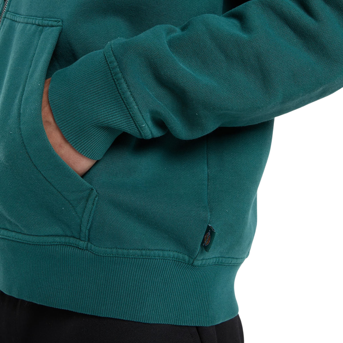 Sweat Dickies Minden em Verde Escuro, close-up do bolso com a mão do modelo, mostrando o punho e a bainha canelados e a etiqueta tecida na costura lateral.
