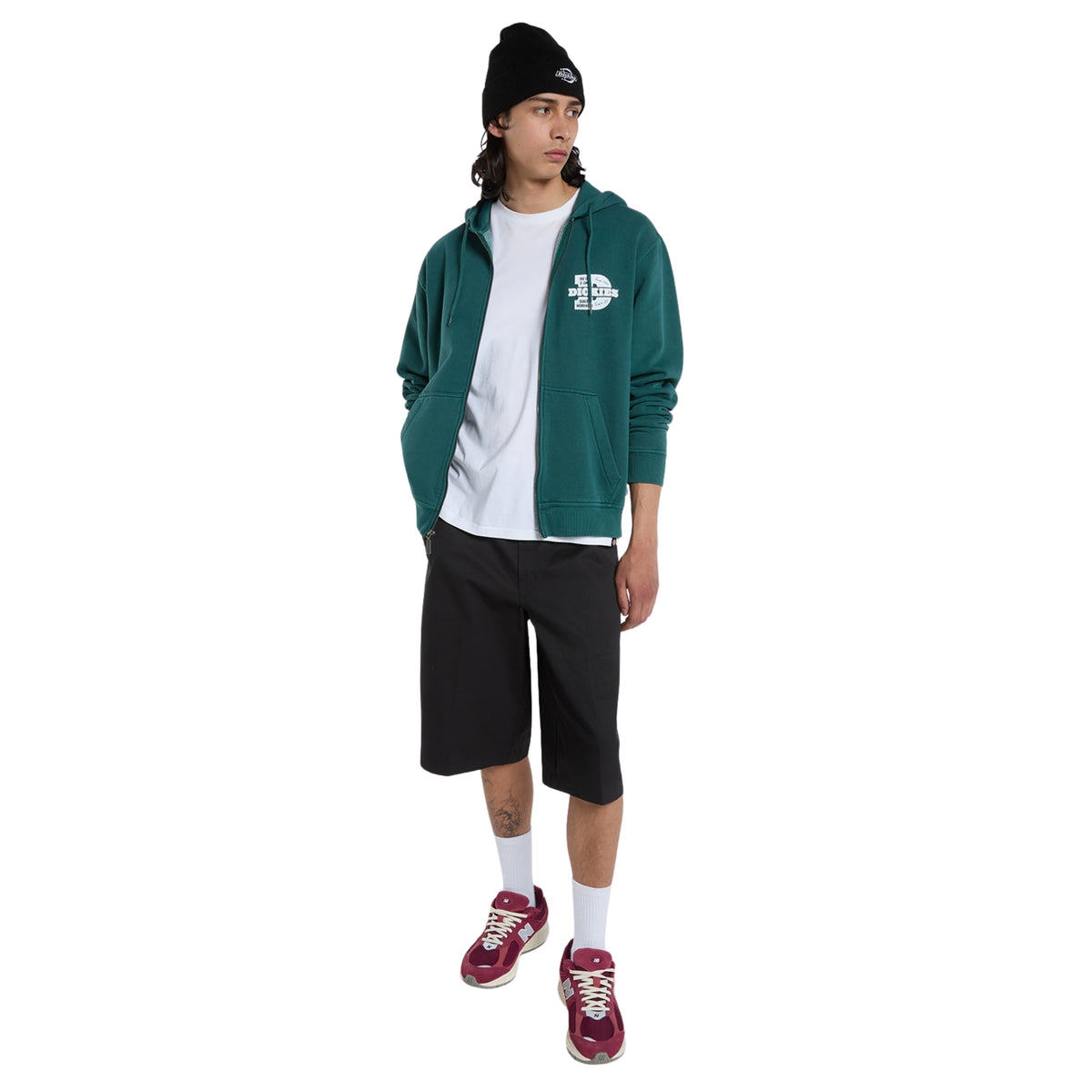 Sweat Dickies Minden em Verde Escuro, vista de corpo inteiro no modelo, usada aberta sobre uma t-shirt branca, com calções e gorro pretos e sapatilhas bordô.