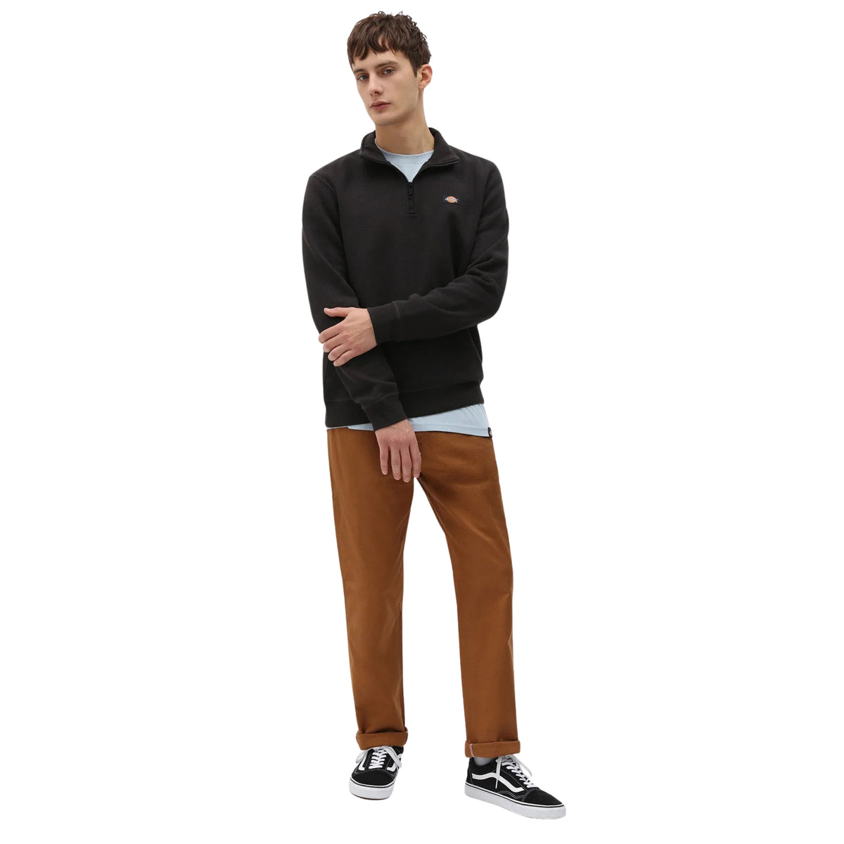Modelo de corpo inteiro com sweat Dickies Oakport preta com meio fecho aberto, t-shirt clara, calças castanhas e sapatilhas pretas e brancas.