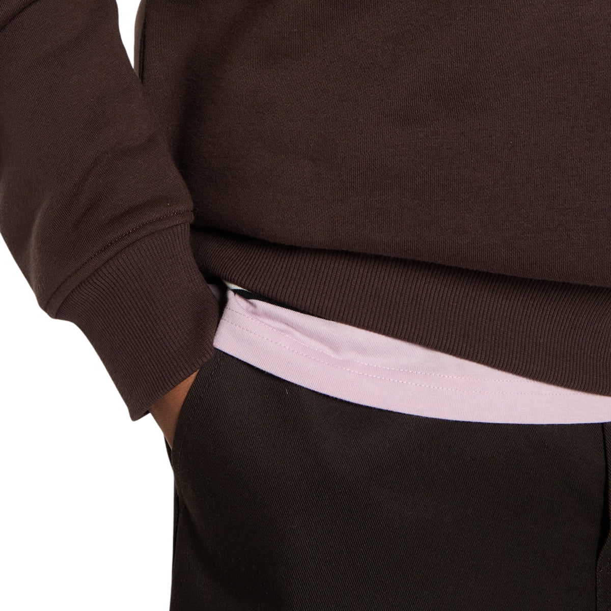 Sweat Dickies Oakport Quarter Zip em Chocolate Brown, close-up do punho e da bainha canelados, com a t-shirt clara visível por baixo e a mão do modelo no bolso dos calções.