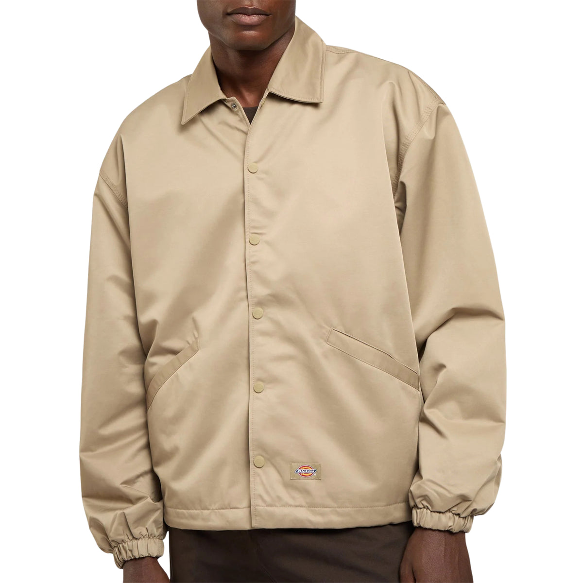 Pormenor frontal do casaco Dickies Parks Khaki, com gola, molas de pressão, bolsos inclinados e etiqueta Dickies junto à bainha.