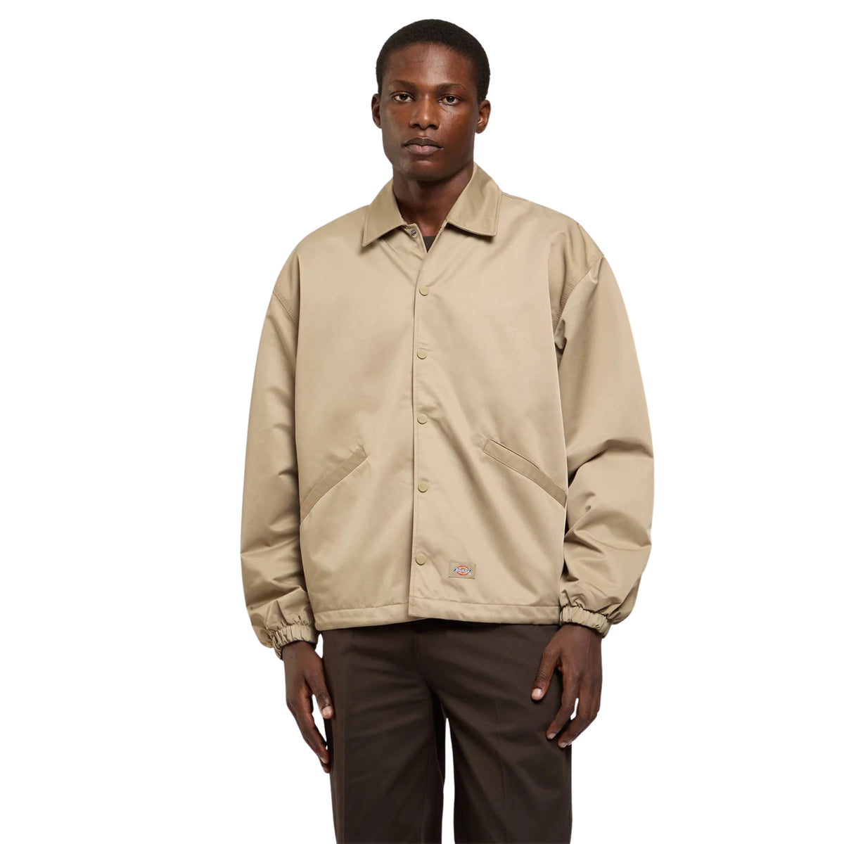 Casaco coach Dickies Parks em Khaki vestido por modelo de frente, fechado com molas de pressão e com bolsos inclinados.