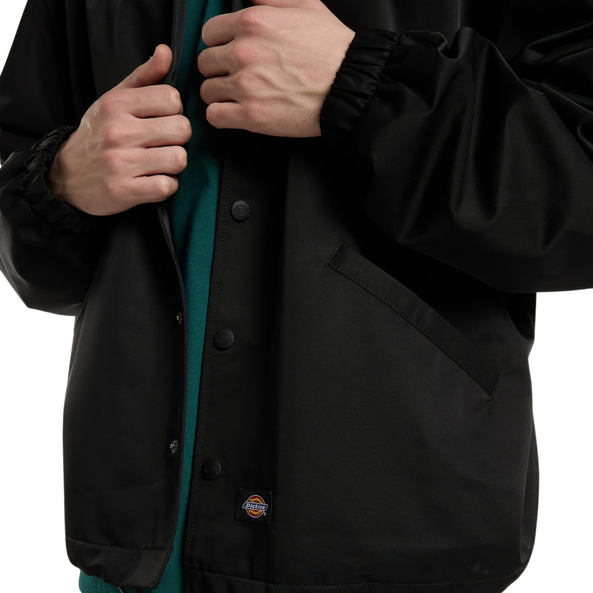 Casaco coach Dickies Parks em Preto, close-up da frente com molas de pressão, bolso de entrada lateral, punhos elásticos e etiqueta tecida Dickies.