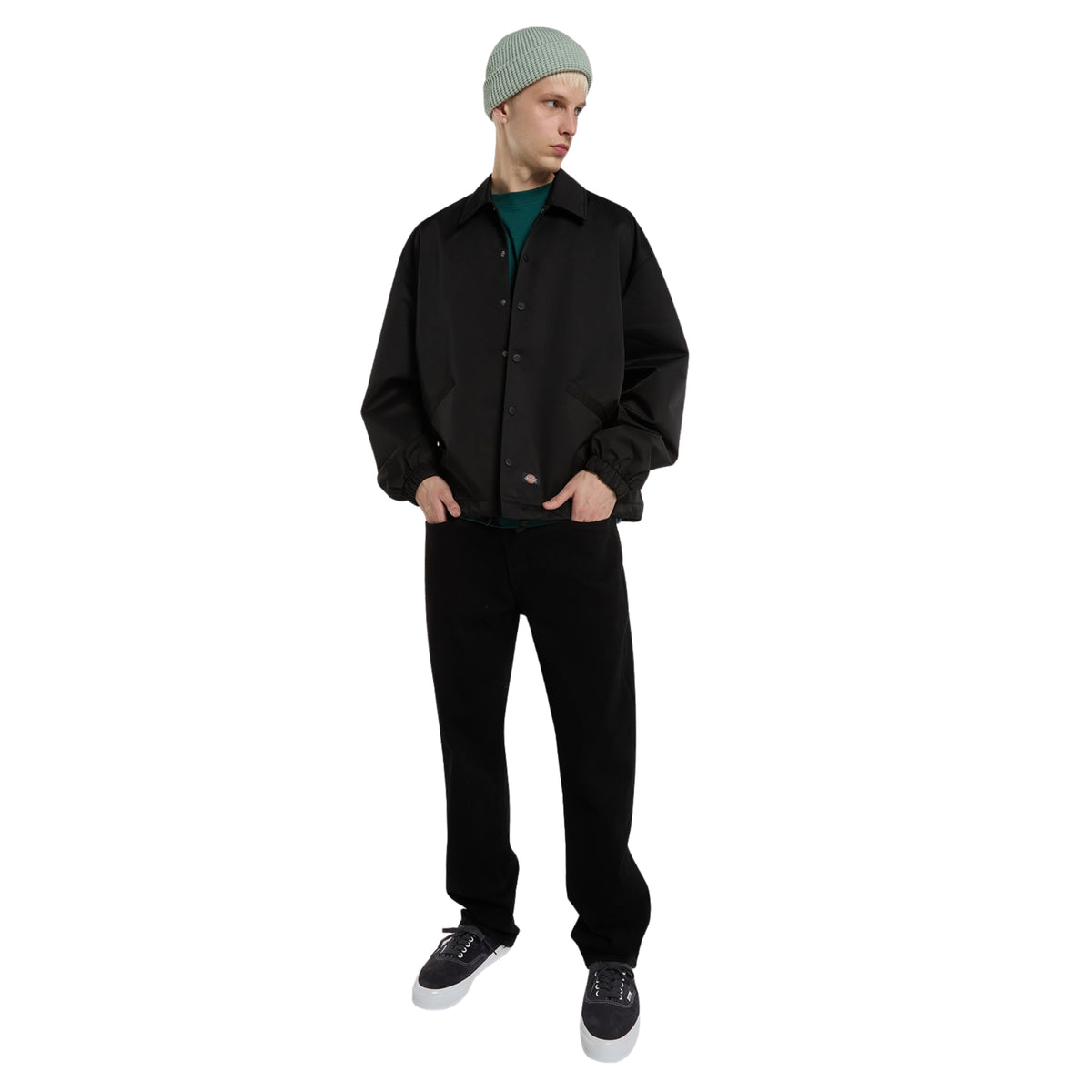 Casaco coach Dickies Parks em Preto, modelo de corpo inteiro com o casaco aberto sobre t-shirt verde, calças pretas e gorro cinzento.