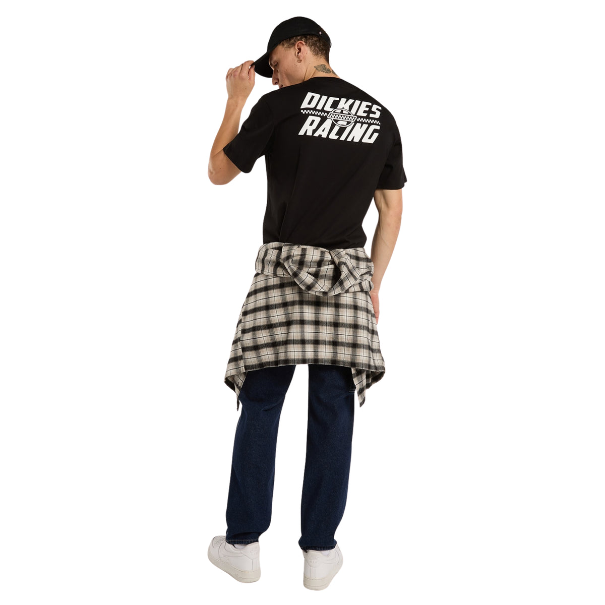 Modelo de corpo inteiro de costas com t-shirt Dickies Racing preta, gráfico branco nas costas, camisa aos quadrados atada à cintura e calças de ganga.