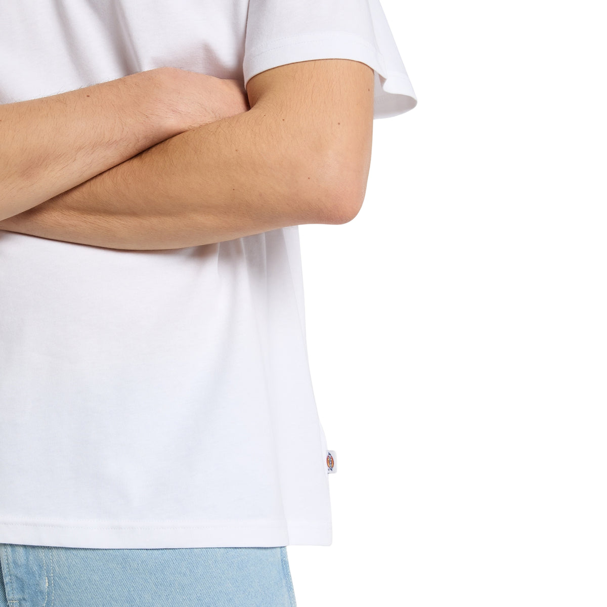 Pormenor da manga curta, bainha e etiqueta Dickies na costura lateral da t-shirt Racing branca, em modelo com braços cruzados.