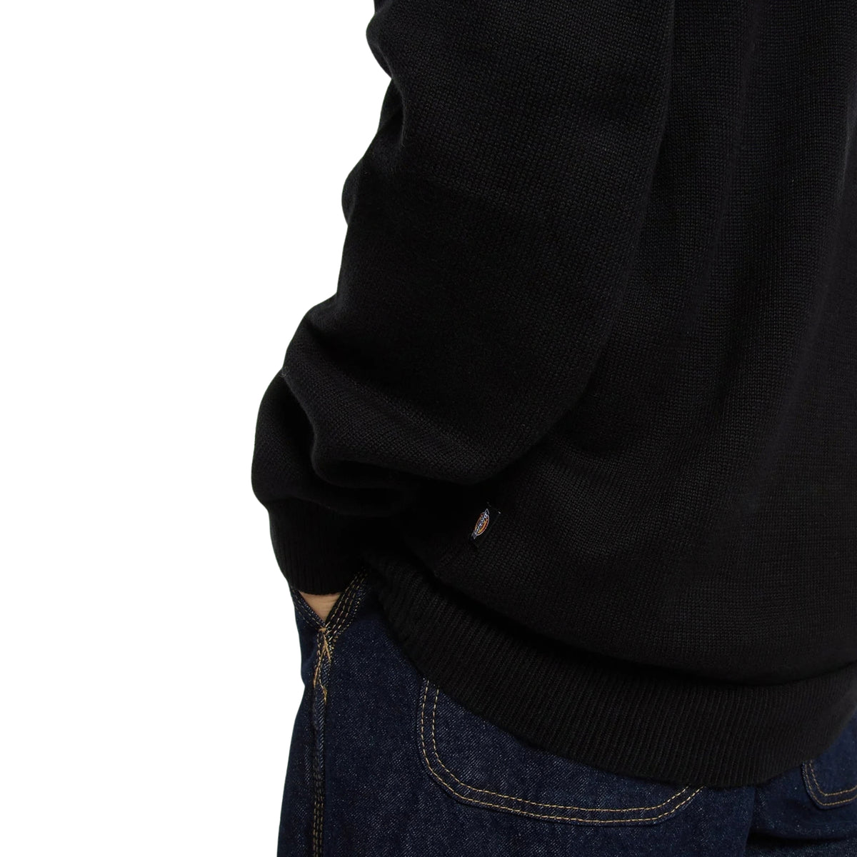Camisola de malha para homem Dickies Summerdale preta — pormenor da bainha canelada e da pequena etiqueta Dickies, junto a calças de ganga azul-escuras.