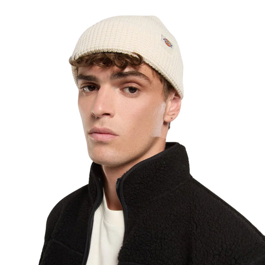 Gorro unissexo Dickies Woodworth Waffle Beanie em Ecru — modelo masculino em plano aproximado com patch bordada Dickies na dobra frontal, vestindo casaco polar preto.
