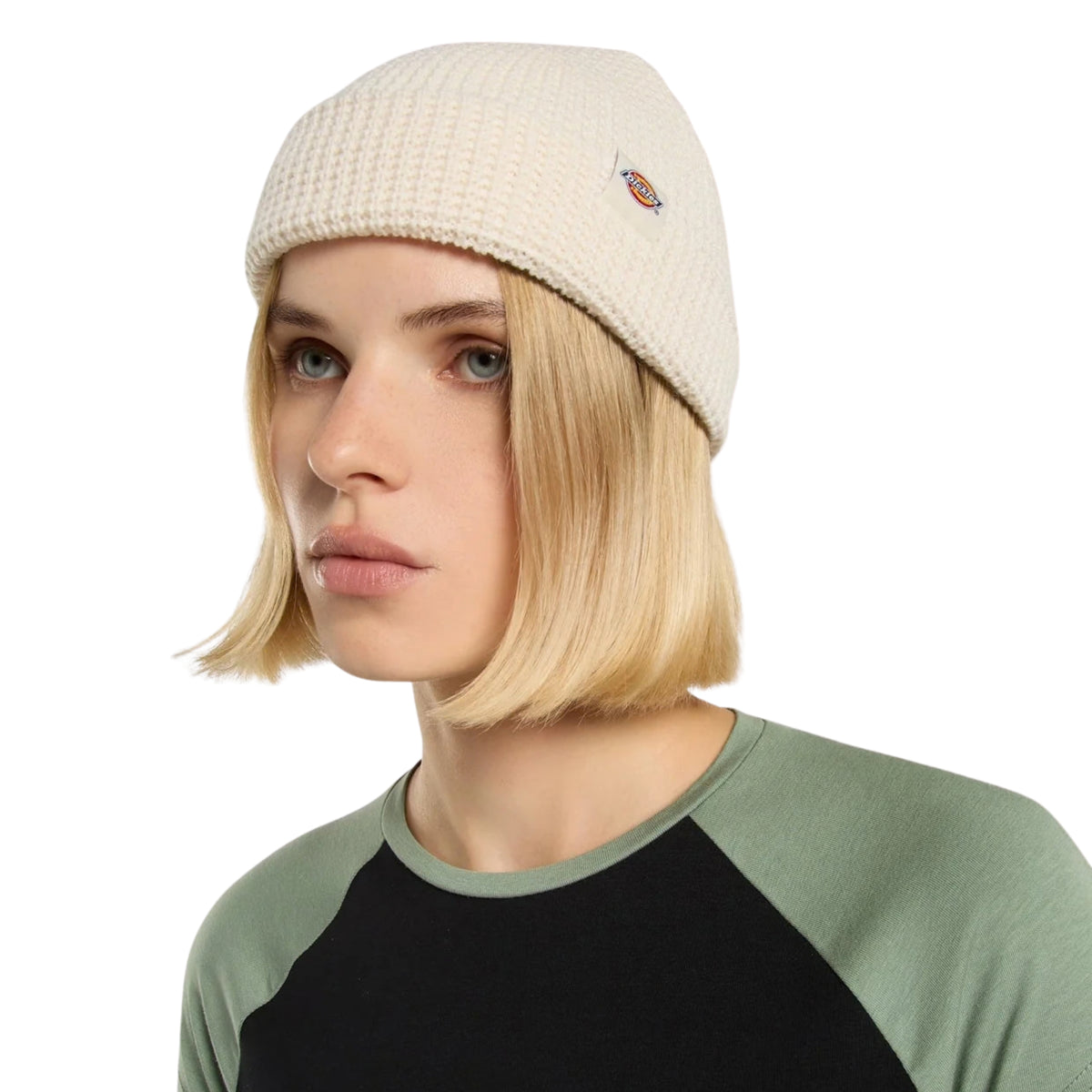 Gorro unissexo Dickies Woodworth Waffle Beanie em Ecru — modelo feminino em plano aproximado com patch bordada Dickies na dobra frontal, vestindo t-shirt raglan verde e preta.
