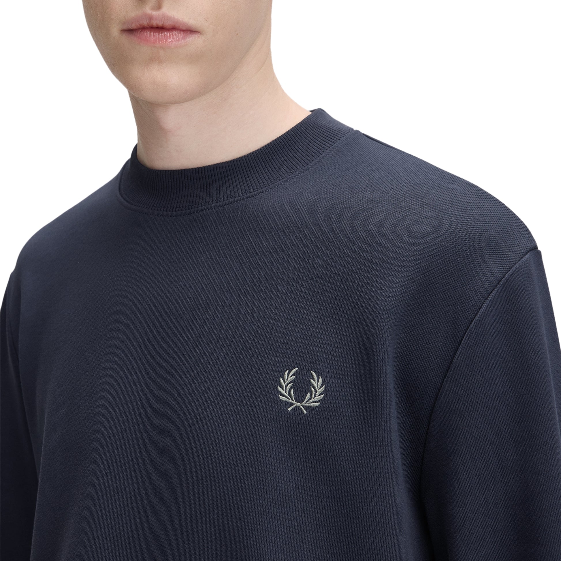 Sweat para homem Fred Perry Crew Neck em Dark Airforce / Ecru / Seagrass — detalhe do twin tipping Ecru/Seagrass nos punhos na proporção 5-4-4 e bordado Laurel Wreath no peito esquerdo, close-up com modelo.