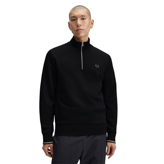 Sweat com meio-fecho Fred Perry Half Zip Sweatshirt em Black — vista frontal com modelo, meio corpo, meio-fecho metálico fechado, bordado Laurel Wreath em Laurel Wreath Green no peito esquerdo, twin tipping Ecru/Laurel Wreath Green nos punhos, combinado com calças navy.