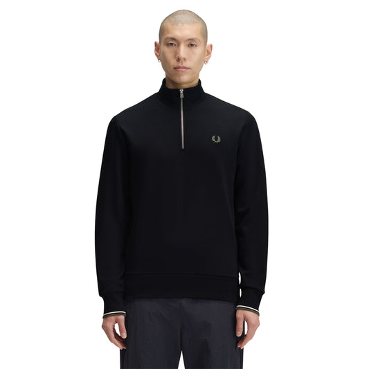 Sweat com meio-fecho Fred Perry Half Zip Sweatshirt em Black — vista frontal com modelo, meio corpo, ângulo ligeiramente diferente, bordado Laurel Wreath em Laurel Wreath Green e twin tipping nos punhos visíveis, combinado com calças navy.