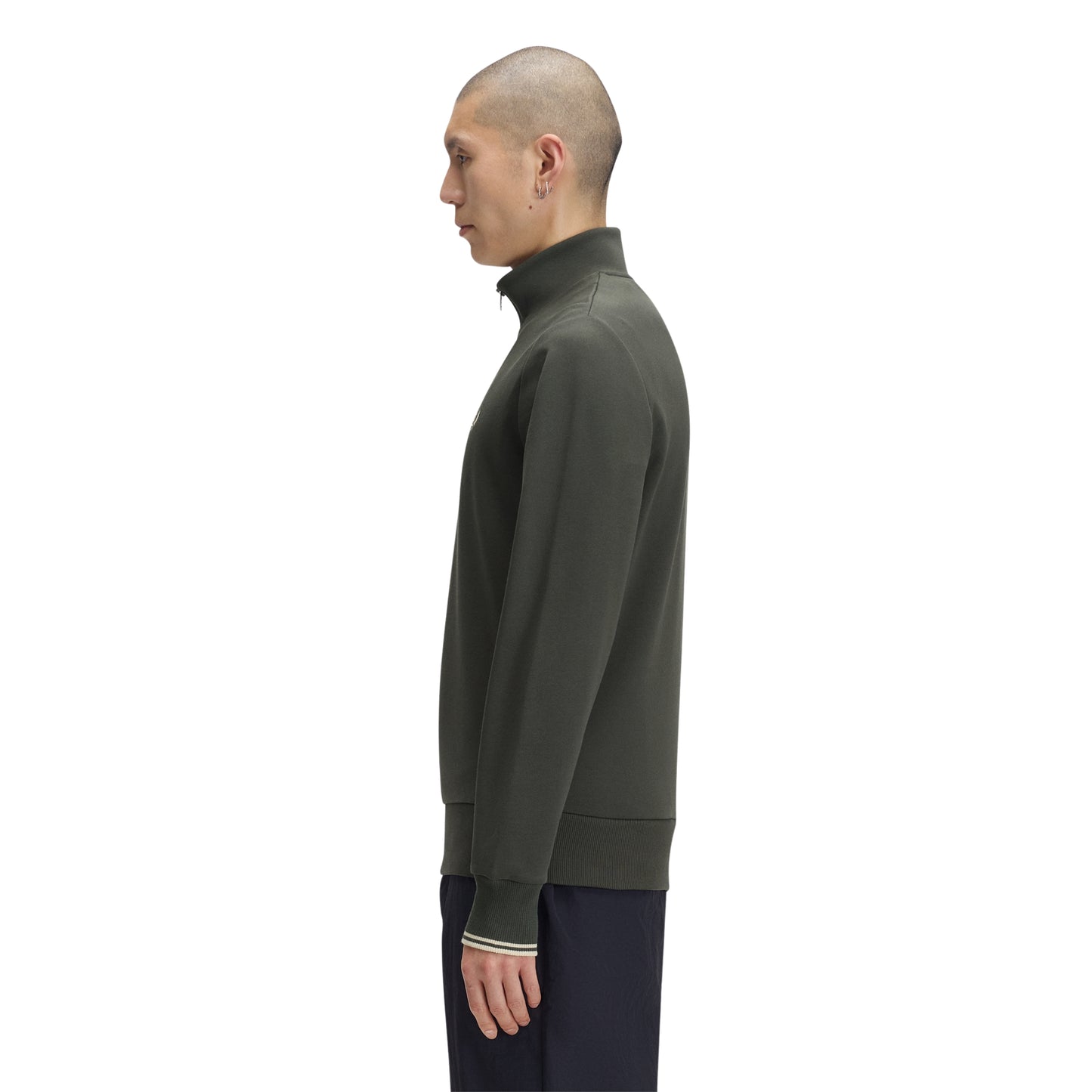 Sweat com meio-fecho Fred Perry Half Zip Sweatshirt em Field Green — vista lateral com modelo, corpo inteiro, perfil do meio-fecho e gola alta visíveis, twin tipping nos punhos, combinado com calças navy Fred Perry.