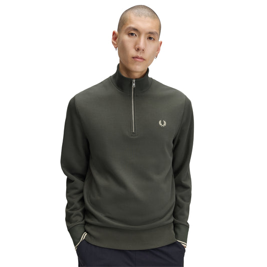 Sweat com meio-fecho Fred Perry Half Zip Sweatshirt em Field Green — vista frontal com modelo, meio corpo, meio-fecho fechado, bordado Laurel Wreath em Oatmeal no peito esquerdo, twin tipping nos punhos, combinado com calças navy Fred Perry.