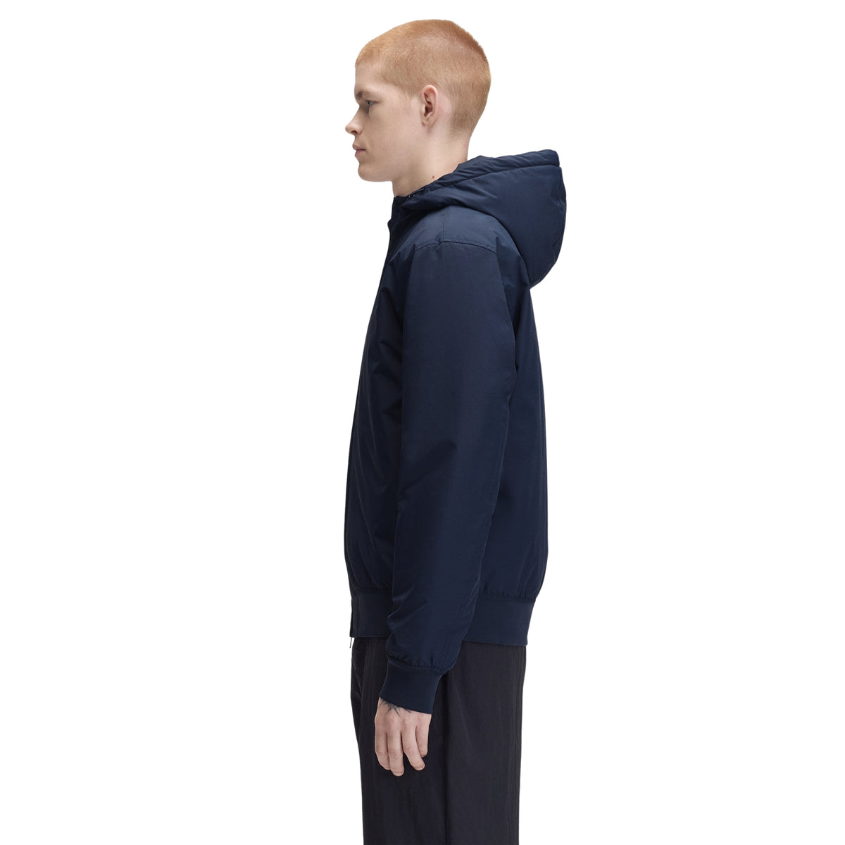 Casaco com carapuço para homem Fred Perry Hooded Brentham Jacket em Dark Airforce — modelo masculino de perfil esquerdo, corpo inteiro, casaco azul-marinha escuro com carapuço volumoso fechado, punho canelado visível, regular fit, calças pretas, fundo branco.