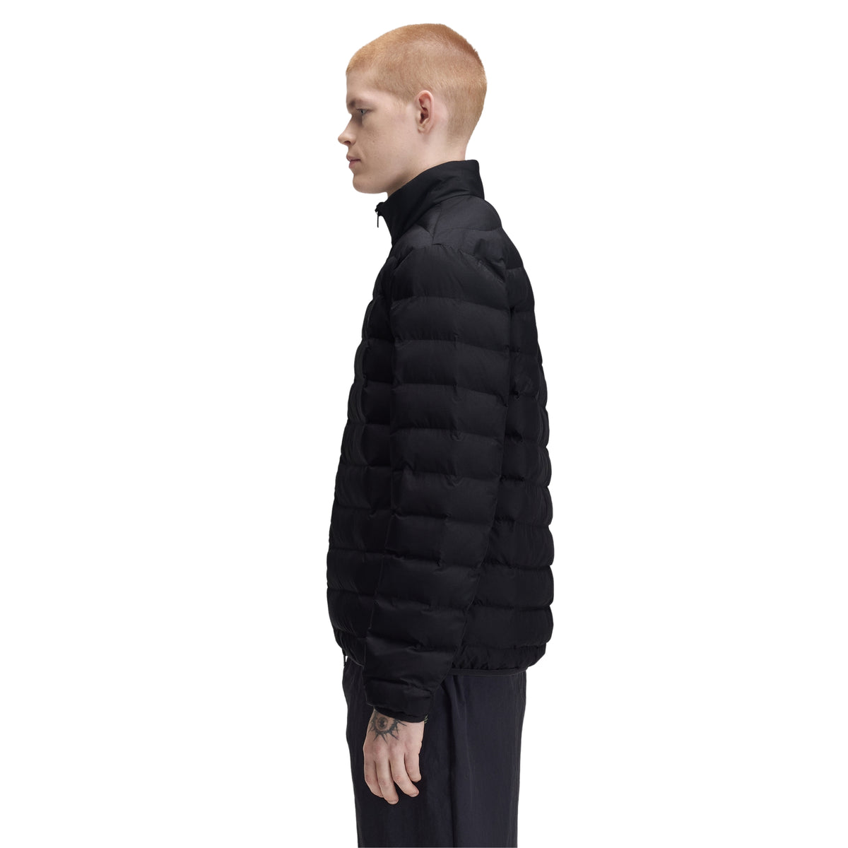 Casaco acolchoado para homem Fred Perry Insulated Jacket em Black — modelo masculino de perfil direito, corpo inteiro, nylon reciclado preto, gola alta com zip visível de perfil, enchimento acolchoado horizontal em todo o corpo e mangas, bolso lateral na costura visível, regular fit, calças pretas, fundo branco.