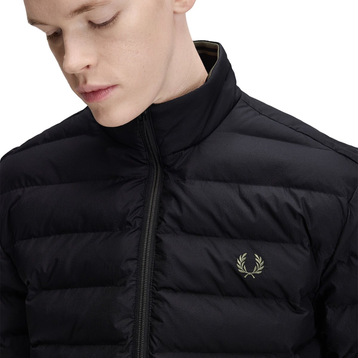 Casaco acolchoado para homem Fred Perry Insulated Jacket em Black — detalhe da gola alta com twin tipping interno caqui visível, zip central preto, nylon reciclado preto, enchimento acolchoado horizontal, logo laurel wreath bordado a caqui no peito esquerdo em close-up, fundo branco.