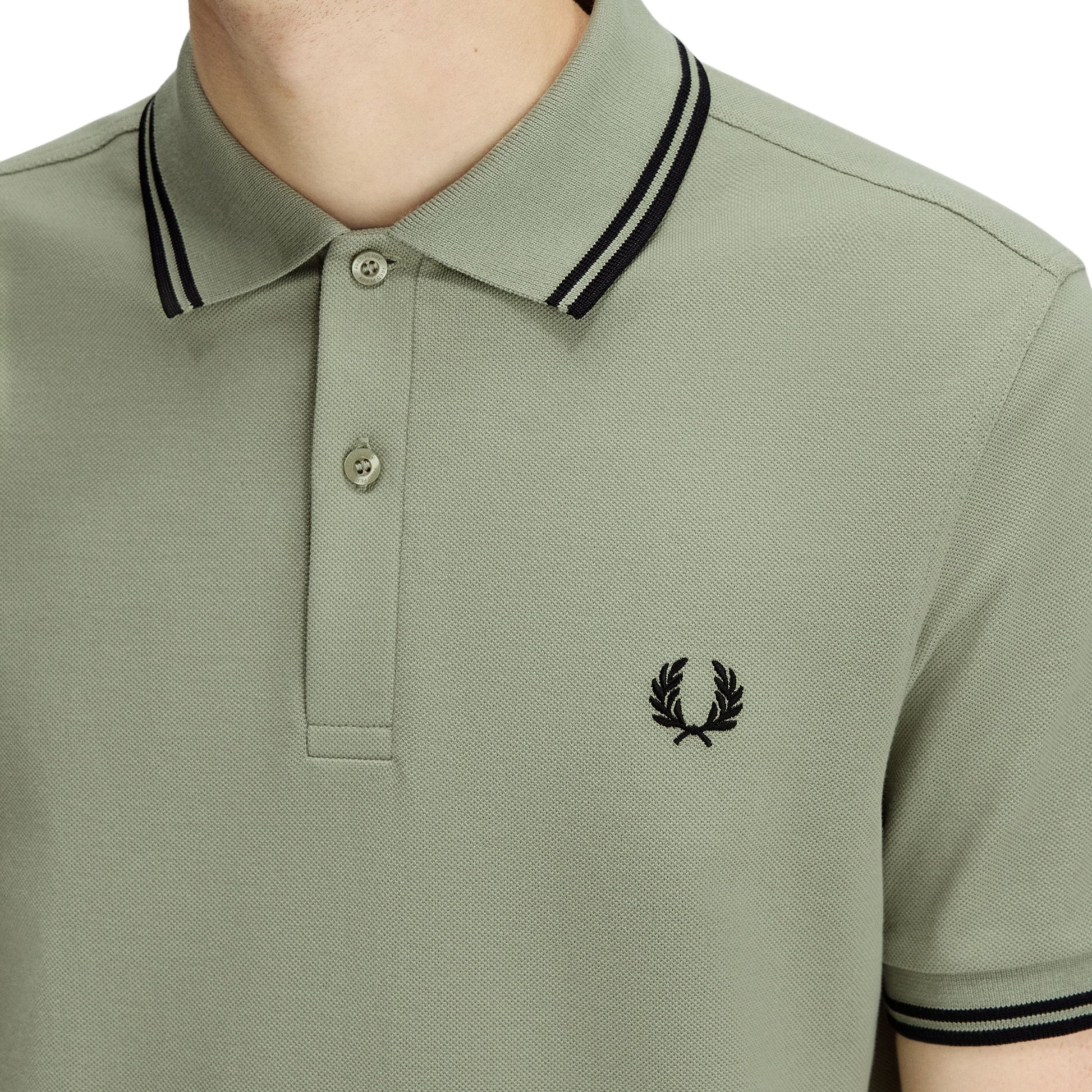 Polo de manga curta para homem Fred Perry M3600 em Seagrass/Preto/Preto. Foto de detalhe da parte da frente, vestido.