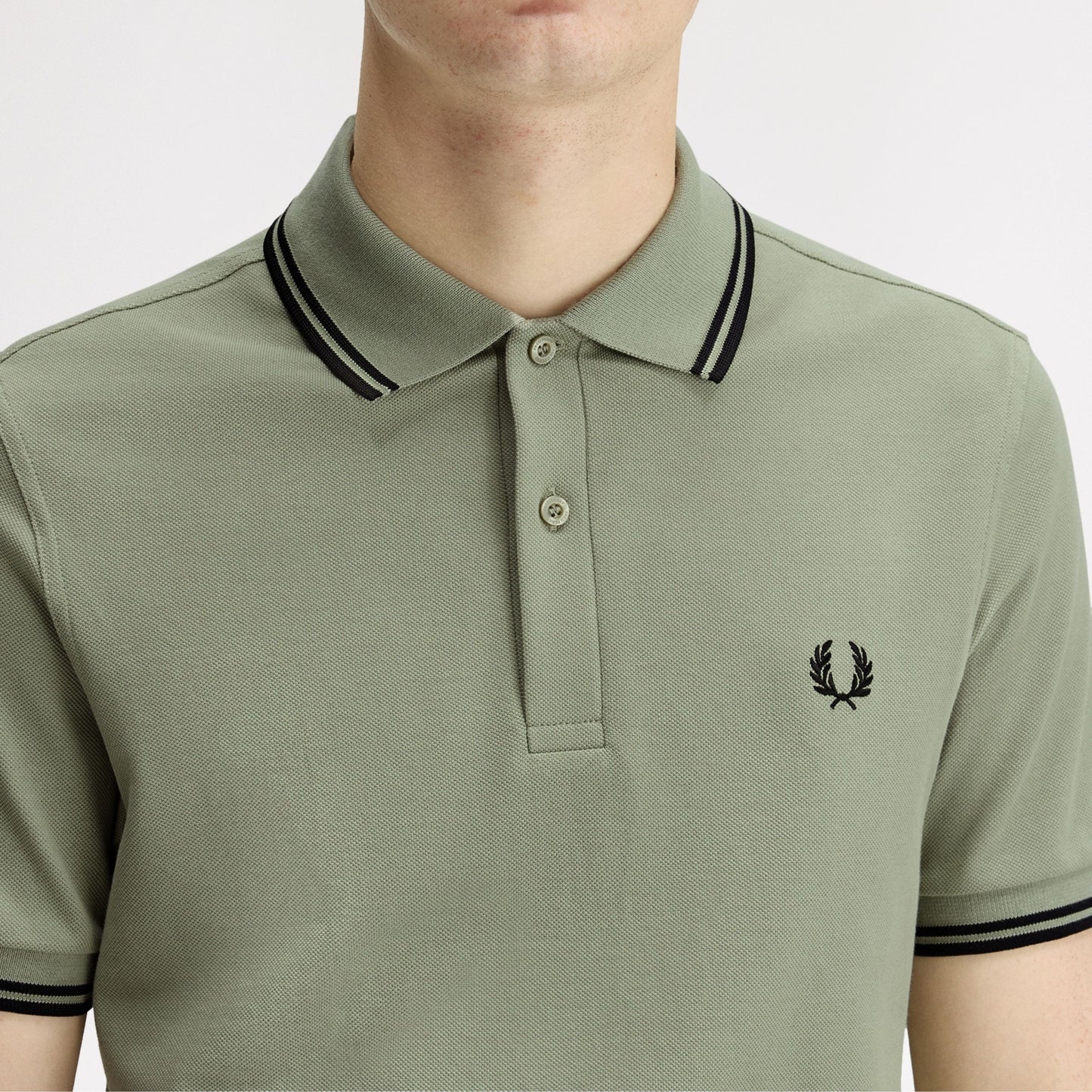 Polo de manga curta para homem Fred Perry M3600 em Seagrass/Preto/Preto. Foto de detalhe da parte da frente, vestido.