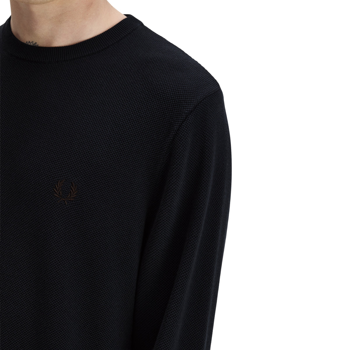Camisola de malha para homem Fred Perry Pique Stitch Jumper em Navy — detalhe do ombro direito e peito, malha piqué azul-marinha escura, logo laurel wreath bordado em tom sobre tom no peito esquerdo, textura piqué do algodão bem visível, gola redonda canelada parcialmente visível, fundo branco.
