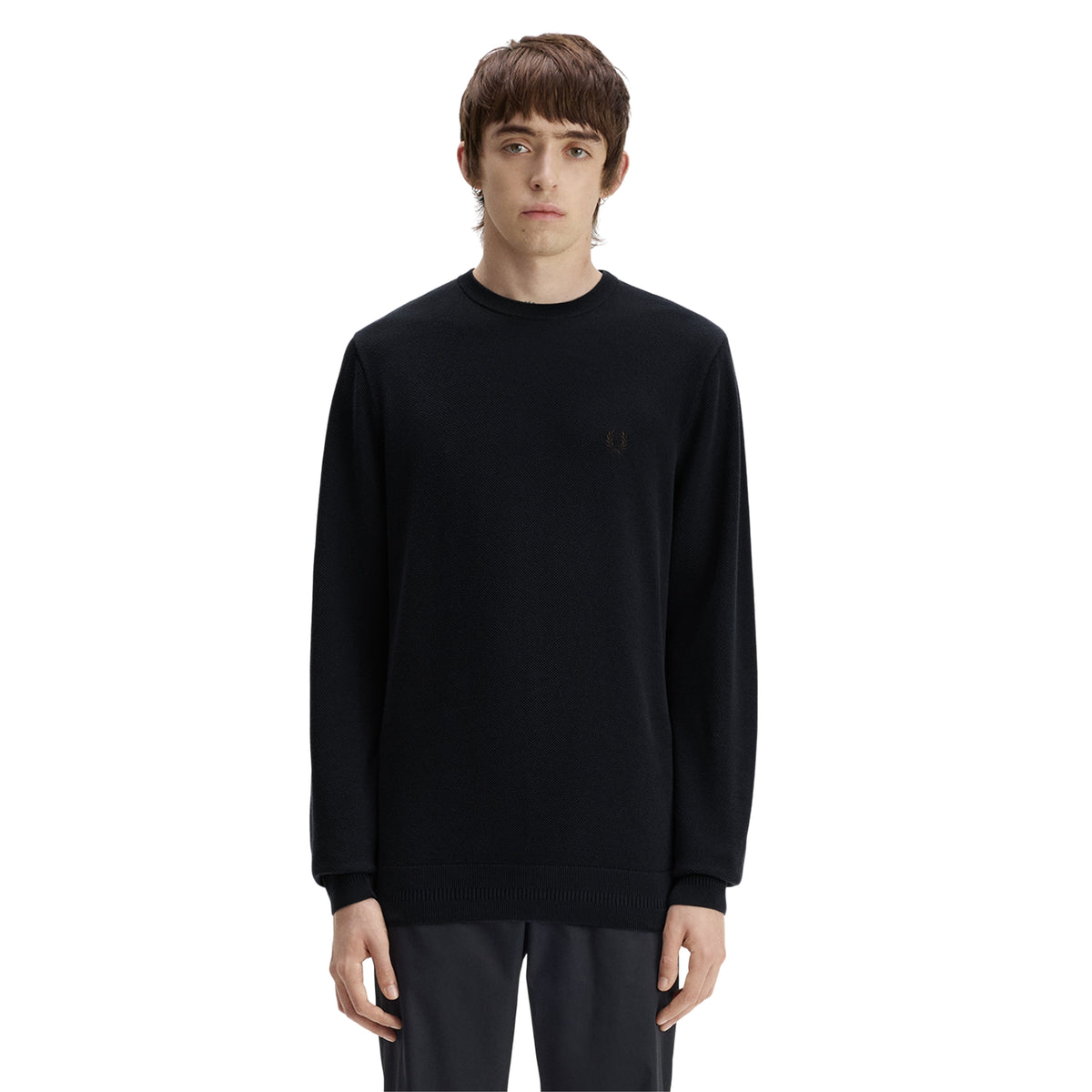 Camisola de malha para homem Fred Perry Pique Stitch Jumper em Navy — modelo masculino de frente, corpo inteiro, malha piqué azul-marinha escura, gola redonda canelada, logo laurel wreath bordado em tom sobre tom no peito esquerdo, barra canelada, regular fit, calças escuras, fundo branco.