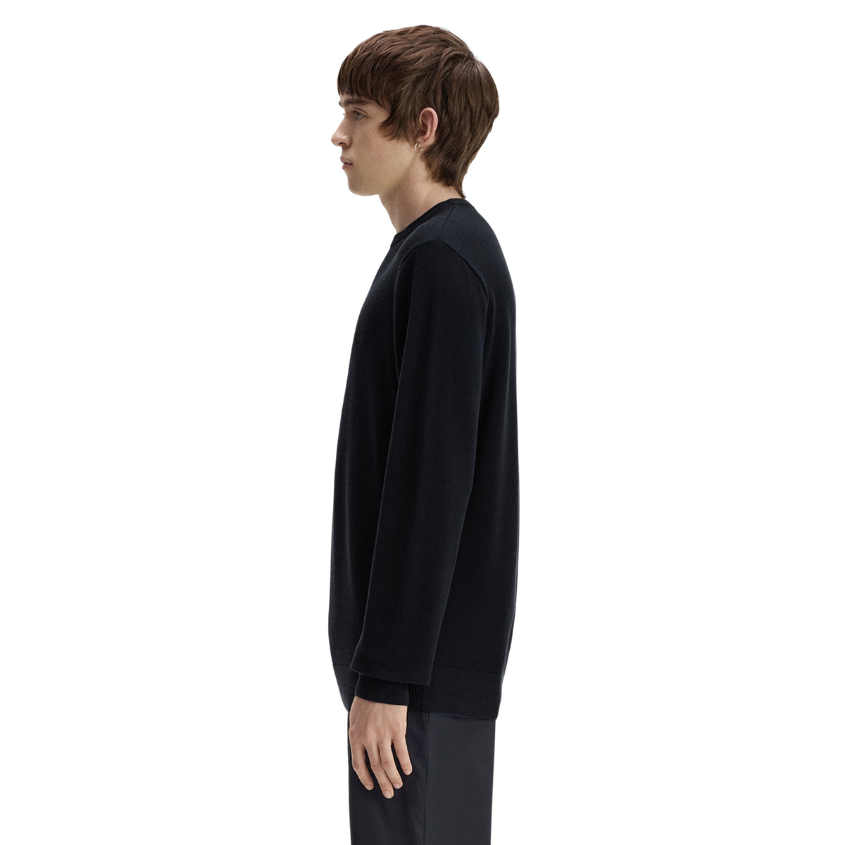 Camisola de malha para homem Fred Perry Pique Stitch Jumper em Navy — modelo masculino de perfil esquerdo, corpo inteiro, malha piqué azul-marinha escura, gola redonda canelada, punho canelado visível, barra canelada, regular fit, calças escuras, fundo branco.