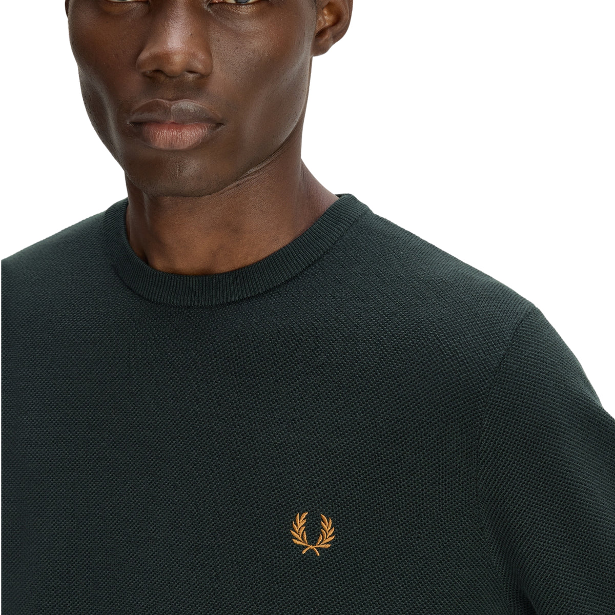 Camisola de malha para homem Fred Perry Pique Stitch Jumper em Night Green — detalhe da gola redonda canelada e peito, malha piqué verde-escuro Night Green, logo laurel wreath bordado a dourado no peito esquerdo em destaque, textura piqué do algodão bem visível, fundo branco.