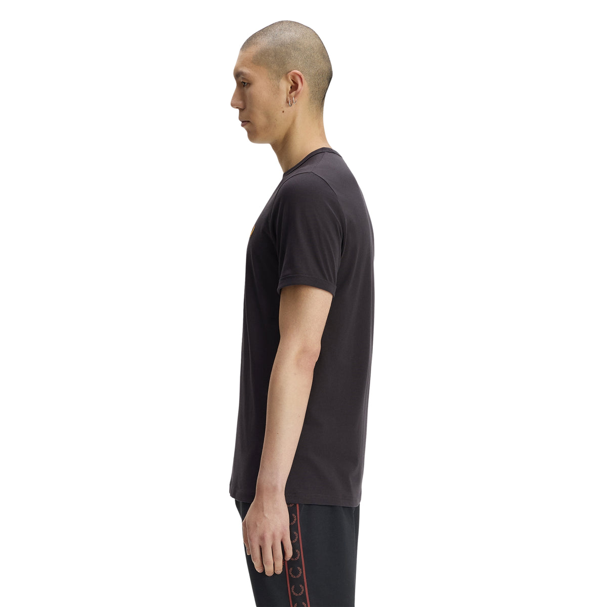 T-shirt de manga curta para homem Fred Perry Ringer T-Shirt em Anchor Grey — modelo masculino de perfil esquerdo, corpo inteiro, jersey cinzento carvão Anchor Grey, gola canelada em contraste visível, regular fit, calças pretas com faixa lateral vermelha, fundo branco.
