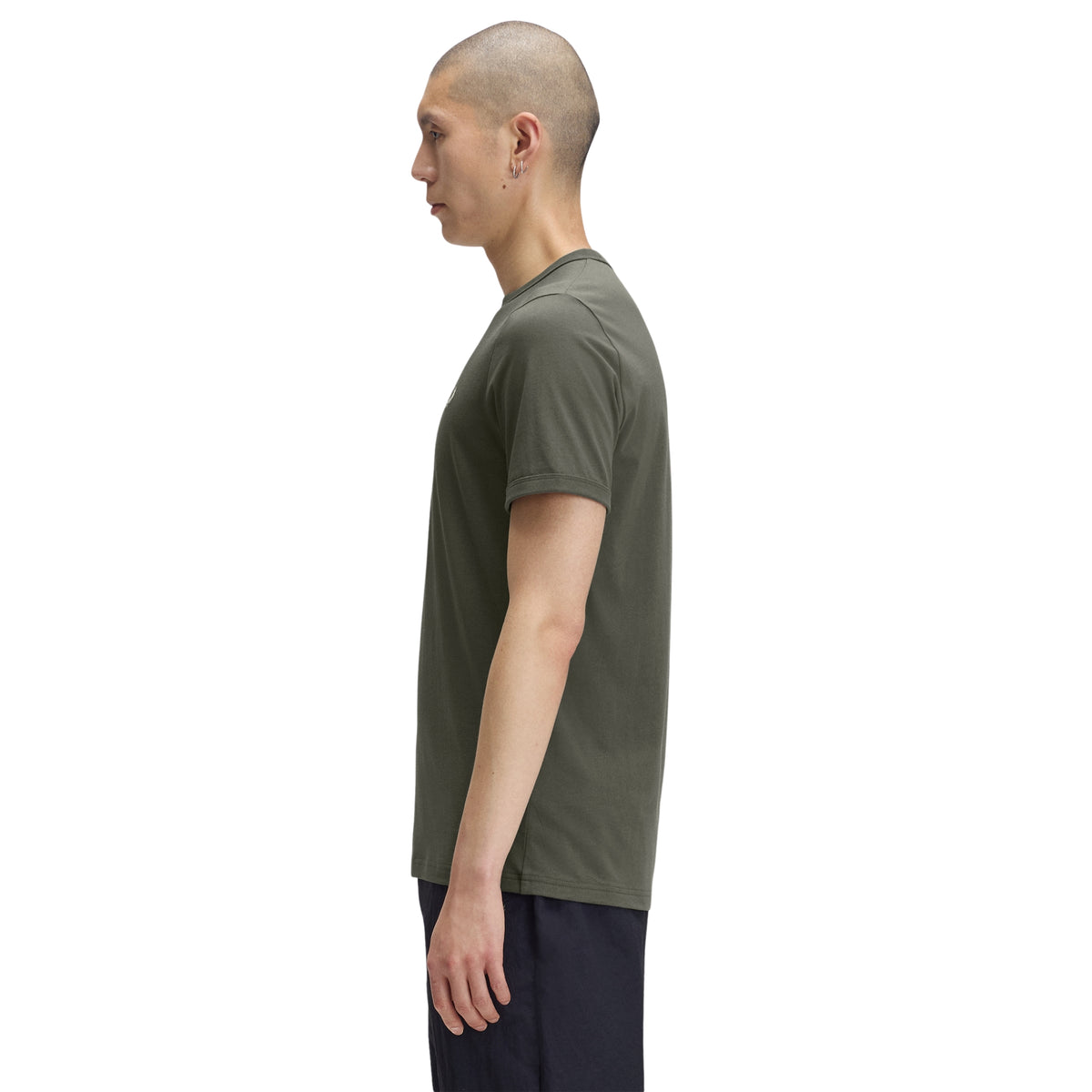 T-shirt de manga curta para homem Fred Perry Ringer T-Shirt em Field Green — modelo masculino de perfil esquerdo, corpo inteiro, jersey verde-musgo Field Green, gola canelada em contraste, punho canelado visível, regular fit, calças azul-marinho, fundo branco.
