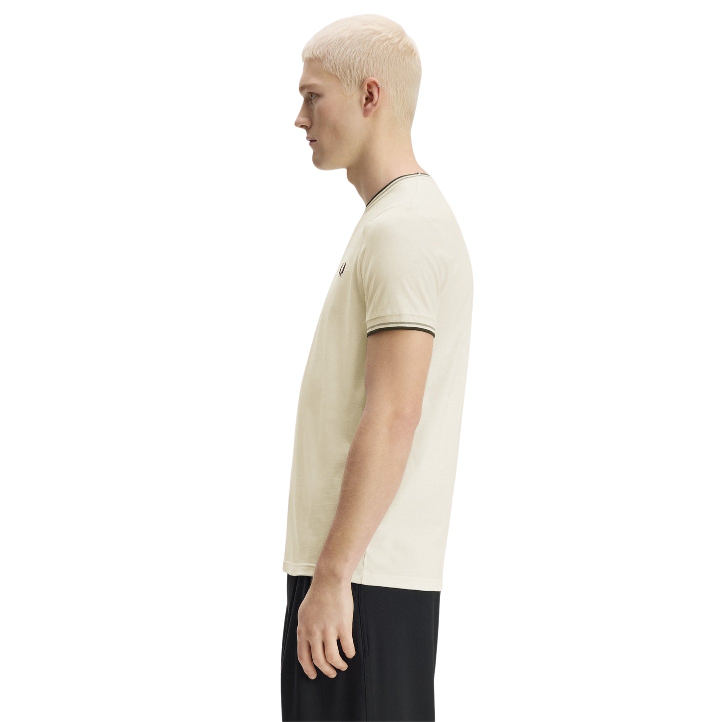 T-shirt Fred Perry Twin Tipped T-Shirt em Ecru — vista lateral com modelo, corpo inteiro, perfil da gola redonda e twin tipping Seagrass/Dark Airforce no colarinho e punho visíveis, combinado com calças pretas.
