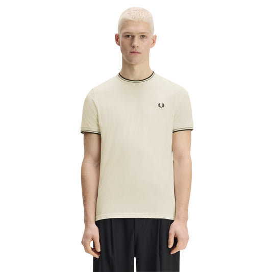 T-shirt Fred Perry Twin Tipped T-Shirt em Ecru — vista frontal com modelo, corpo inteiro, braços ao longo do corpo, bordado Laurel Wreath em Dark Airforce e twin tipping no colarinho e punhos visíveis, combinado com calças pretas.